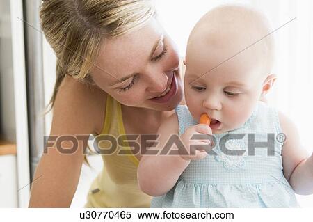 Mother and baby in kitchen eating carrot View Large Photo Image Stock Photography - Mother and baby in kitchen eating carrot. Fotosearch