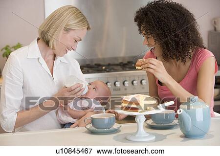 Mother and baby in kitchen with friend eating cake and smiling View Large Photo Image Stock Photo - Mother and baby in kitchen with friend eating cake and smiling. Fotosearch
