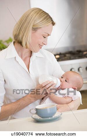 Picture - Mother feeding baby in kitchen with coffee smiling. Fotosearch