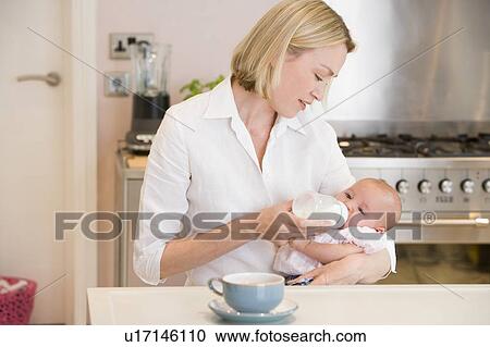 Mother feeding baby in kitchen with coffee View Large Photo Image Stock Image - Mother feeding baby in kitchen with coffee. Fotosearch
