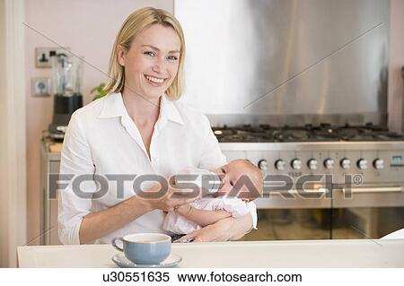 Stock Photography - Mother feeding baby in kitchen with coffee smiling. Fotosearch
