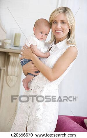 Stock Image - Mother in living room holding baby smiling. Fotosearch