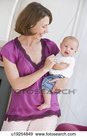 Mother in living room holding baby smiling View Large Photo Image Stock Photo - Mother in living room holding baby smiling. Fotosearch