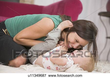 Mother in living room playing with baby smiling View Large Photo Image Stock Photo - Mother in living room playing with baby smiling. Fotosearch