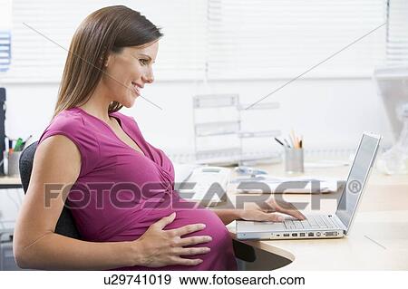 Pregnant woman at work using laptop and smiling View Large Photo Image Stock Photo - Pregnant woman at work using laptop and smiling. Fotosearch