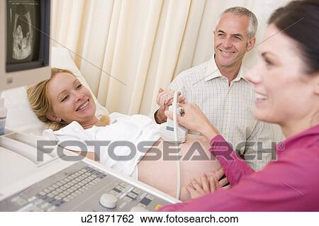 Stock Image - Pregnant woman getting ultrasound from doctor with husband watching. Fotosearch