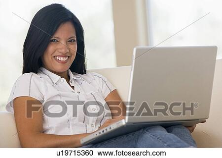 Stock Image - Woman in living room using laptop smiling. Fotosearch