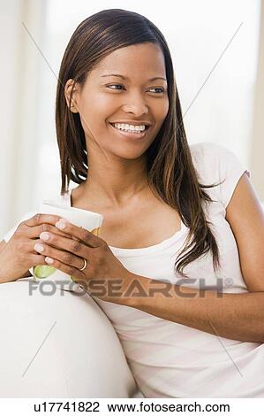 Stock Image - Woman in living room with coffee smiling. Fotosearch