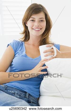 Stock Image - Woman in living room with coffee smiling. Fotosearch
