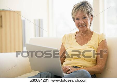 Stock Image - Woman in living room with laptop smiling. Fotosearch