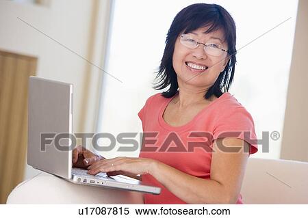 Stock Photography - Woman in living room with laptop smiling. Fotosearch