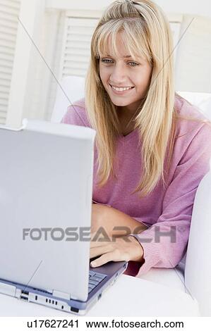 Stock Image - Woman on patio using laptop smiling. Fotosearch