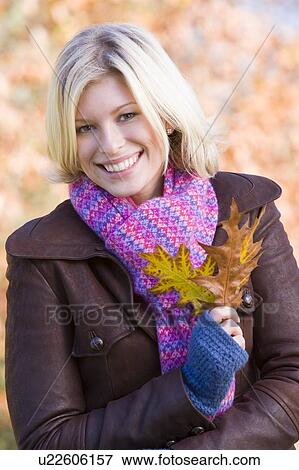 Stock Photo - Woman outdoors at park holding leaves in hand smiling (selective focus). Fotosearch
