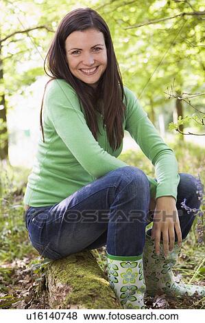 Stock Photo - Woman outdoors in woods sitting on log smiling. Fotosearch