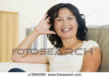 Stock Photography - Woman sitting in living room laughing. Fotosearch