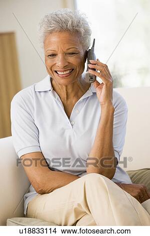 Picture - Woman sitting in living room using telephone and smiling. Fotosearch
