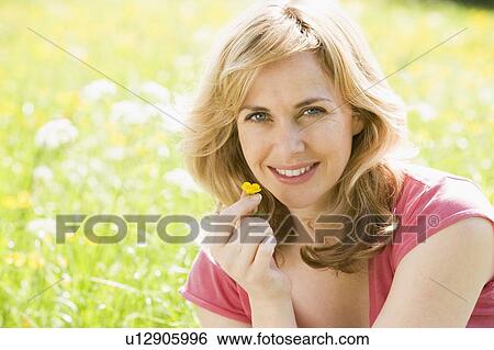 Stock Photograph - Woman sitting outdoors holding flower smiling. Fotosearch
