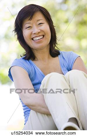 Picture - Woman sitting outdoors smiling. Fotosearch