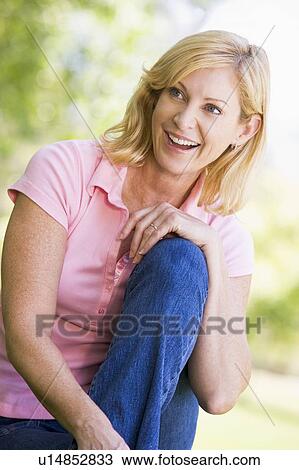 Stock Image - Woman sitting outdoors smiling. Fotosearch