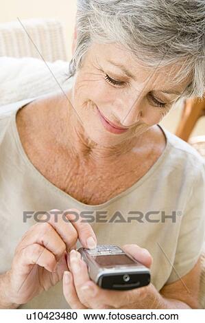 Stock Image - Woman using cellular phone indoors smiling. Fotosearch