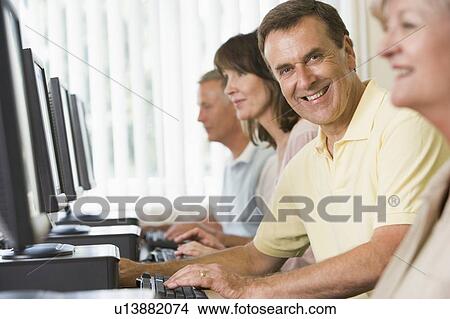 Four people sitting at computer terminals (selective focus/high key) View Large Photo Image Picture - Four people sitting at computer terminals (selective focus/high key). Fotosearch