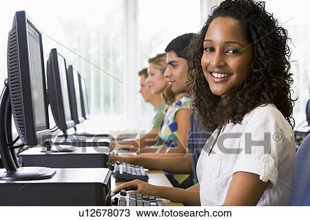 Stock Image - Four people sitting at computer terminals (depth of field/high key). Fotosearch