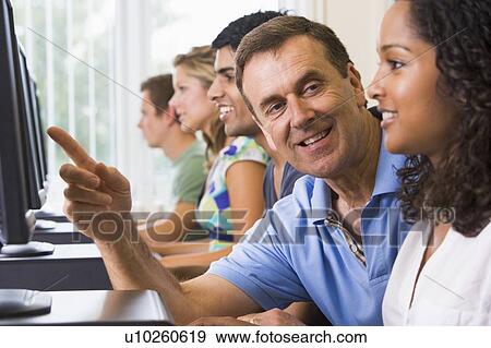 Four students sitting at computer terminals with teacher helping one of them (depth of field/high key) View Large Photo Image Stock Photo - Four students sitting at computer terminals with teacher helping one of them (depth of field/high key). Fotosearch