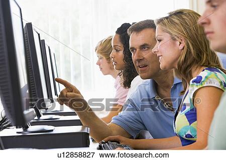Four students sitting at computer terminals with teacher helping one of them (depth of field/high key) View Large Photo Image Stock Photo - Four students sitting at computer terminals with teacher helping one of them (depth of field/high key). Fotosearch
