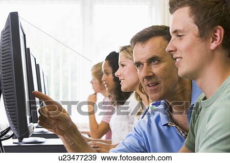 Stock Photo - Four students sitting at computer terminals with teacher helping one of them (depth of field/high key) . Fotosearch