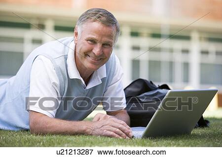 Man lying on lawn of school with laptop View Large Photo Image Stock Photo - Man lying on lawn of school with laptop. Fotosearch