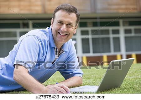 Man lying on lawn of school with laptop View Large Photo Image Stock Photo - Man lying on lawn of school with laptop. Fotosearch