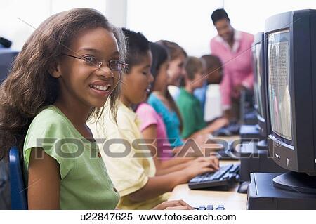 Stock Photography - Six children at computer terminals with teacher in background (depth of field/high key). Fotosearch