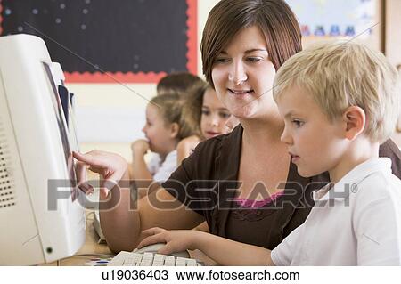 Stock Image - Students in class at computer terminals with teacher (selective focus). Fotosearch
