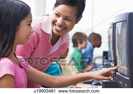 Teacher helping student at computer terminal with students in background (depth of field/high key) View Large Photo Image Stock Image - Teacher helping student at computer terminal with students in background (depth of field/high key). Fotosearch
