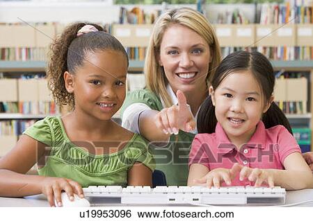Stock Photograph - Two students in class at computer keyboard with teacher. Fotosearch