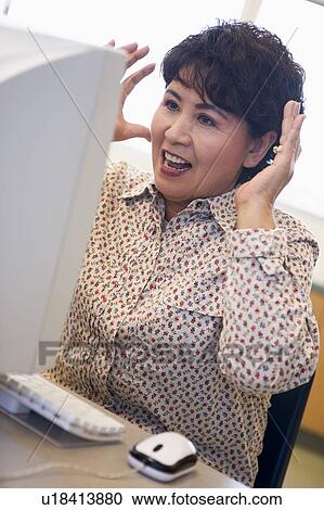Stock Image - Woman at computer looking at monitor surprised (high key). Fotosearch