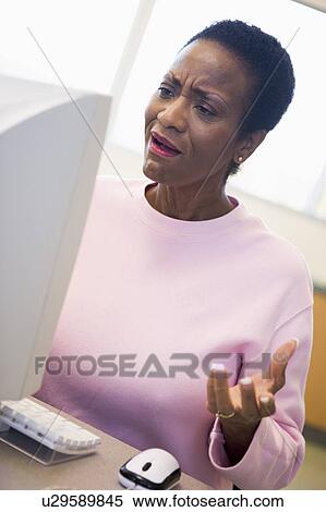 Stock Photography - Woman at computer looking at monitor frustrated (high key). Fotosearch
