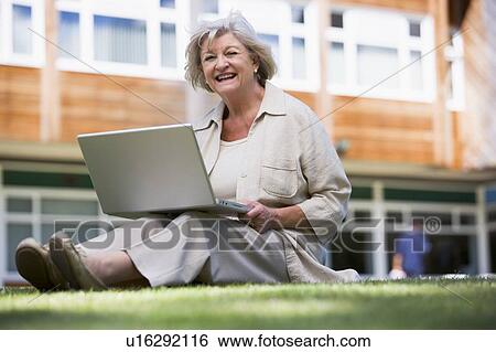 Stock Photograph - Woman sitting on lawn of school with laptop. Fotosearch