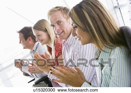 Stock Image - Four businesspeople applauding indoors smiling. Fotosearch