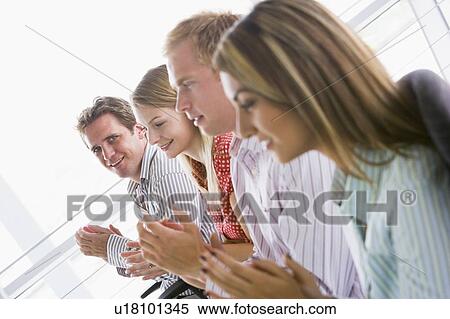 Stock Photography - Four businesspeople applauding indoors smiling. Fotosearch