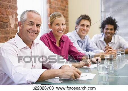 Stock Image - Four businesspeople in boardroom smiling. Fotosearch