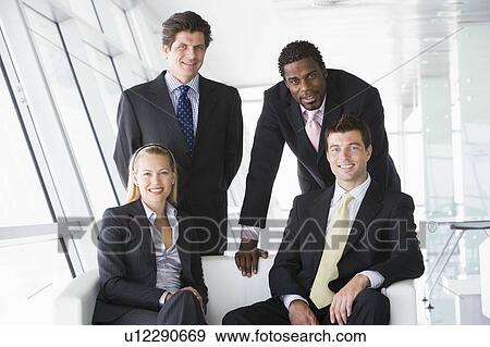 Stock Photo - Four businesspeople in office lobby smiling. Fotosearch