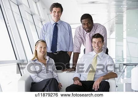 Stock Photograph - Four businesspeople in office lobby smiling. Fotosearch