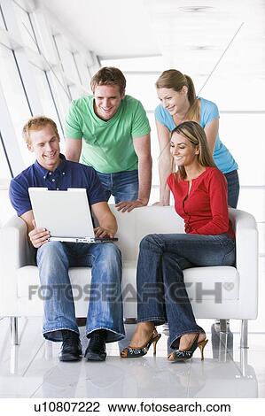 Four people in lobby looking at laptop smiling View Large Photo Image Stock Image - Four people in lobby looking at laptop smiling. Fotosearch