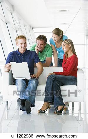 Stock Photograph - Four people in lobby looking at laptop smiling. Fotosearch
