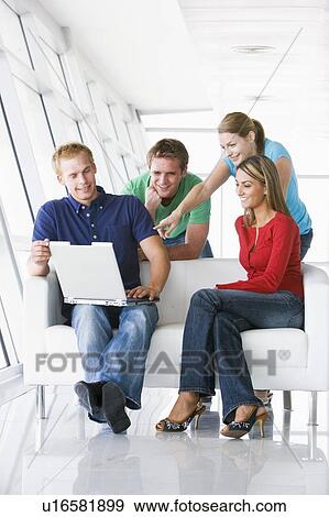 Stock Photo - Four people in lobby pointing at laptop smiling. Fotosearch