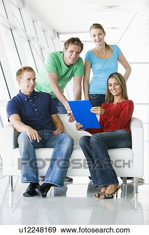 Stock Photo - Four people in lobby pointing at clipboard smiling. Fotosearch