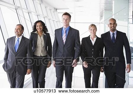 Stock Image - Group of co-workers walking in office space smiling (high key). Fotosearch