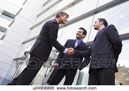 Three businessmen standing outdoors by building shaking hands and smiling (high key/selective focus) View Large Photo Image Stock Photography - Three businessmen standing outdoors by building shaking hands and smiling (high key/selective focus). Fotosearch