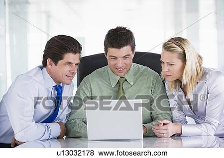 Stock Photo - Three businesspeople in a boardroom looking at laptop. Fotosearch